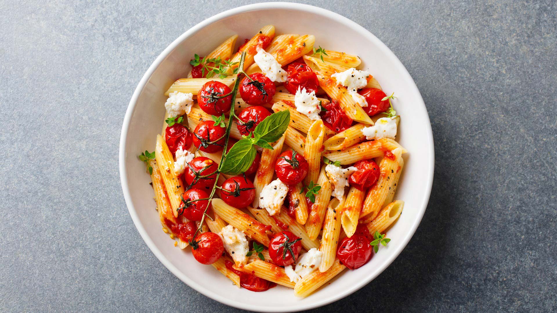 Teller mit Penne, gebackenen Tomaten, cremigem Käse und frischem Basilikum